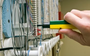 A man connecting wires on a punch block with a punch tool.